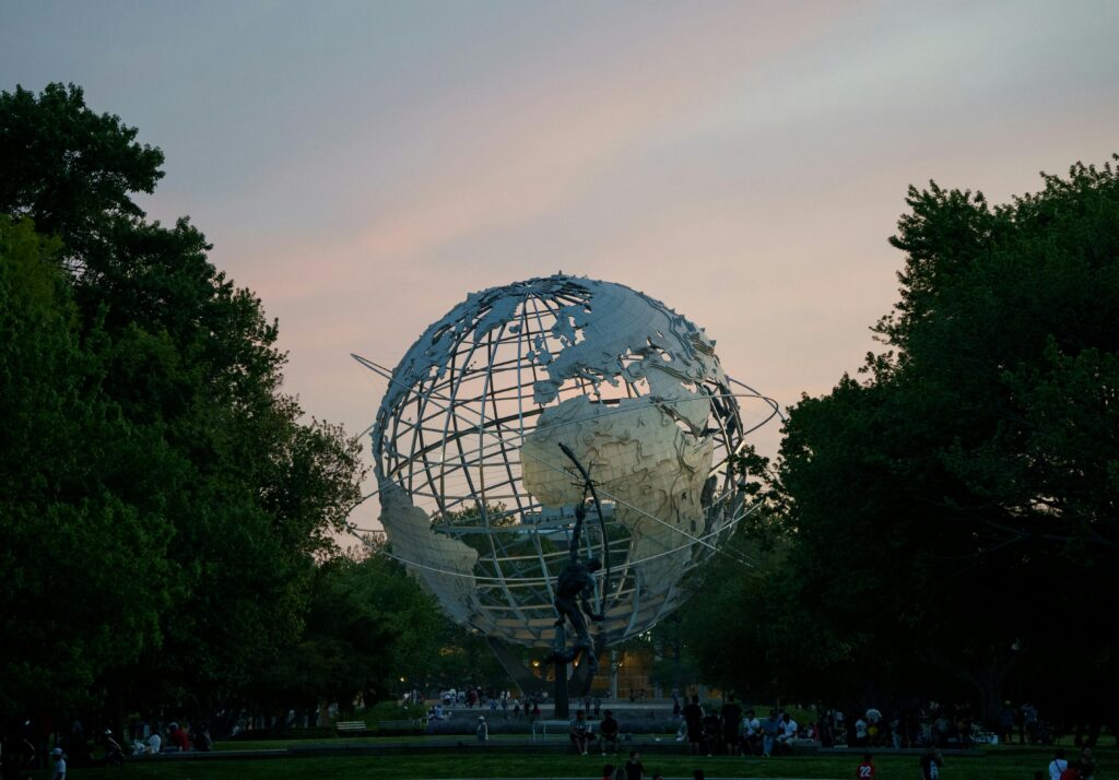 The iconic Unisphere in Queens, New York captured at sunset, surrounded by lush trees and visitors.